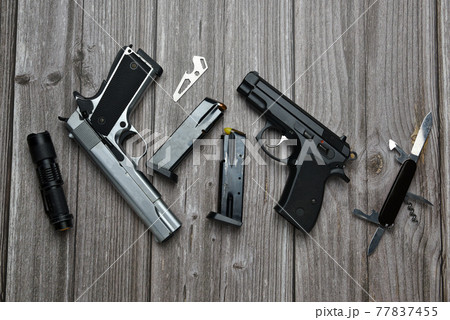 Still life of black and silver handgun with cartridge magazine, flashlight, small knife and multipurpose tool on old grungy brown wooden background, Black and silver semi-automatic with various tools 77837455