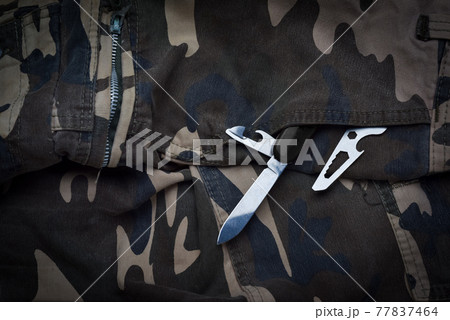 Still life of black and chrome multifunctional pocket tool and small knife on camouflage soldier pant, various tactical tools for defense and survive 77837464