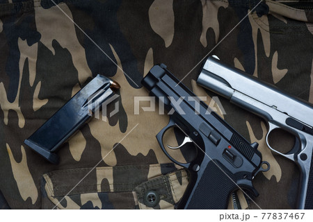 Still life with black and silver handgun with cartridge magazine on camouflage soldier pant background, Black and chrome semi-automatic pistol on camouflage soldier pant Still life with black and silver handgun with cartridge magazine on camouflage soldier pant background, Black and chrome semi-automatic pistol on camouflage soldier pant 77837467