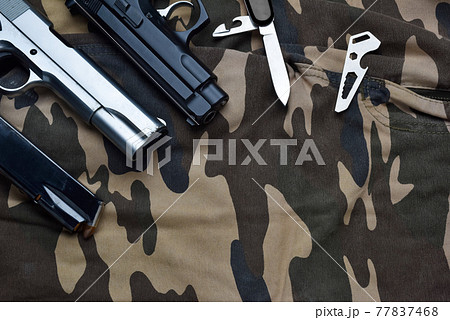 Still life of black and chrome handgun with cartridge magazine, small knife and multifunctional pocket tool on camouflage soldier pant, various tactical weapon and tools for defense Still life of black and chrome handgun with cartridge magazine, small knife and multifunctional pocket tool on camouflage soldier pant, various tactical weapon and tools for defense 77837468