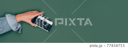 Banner with female hand holding old retro photo camera on green background with copy space for text. Trendy vintage photography, Online photography school concept. Selective focus Banner with female hand holding old retro photo camera on green background with copy space for text. Trendy vintage photography, Online photography school concept. Selective focus 77838753