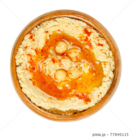 Hummus dip with paprika powder and oil, in a wooden bowl. Middle Eastern dip, spread or savory dish made of cooked, mashed chickpeas, blended with tahini, lemon juice and garlic. Close-up, food photo. 77840115