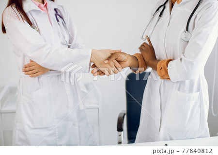 Healthcare, agreement and hiring concept. Two unrecognizable professional multiracial diverse female doctors handshaking at modern hospital, hands close up. 77840812
