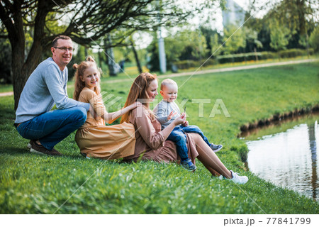 happy family on the bank near the river in summer in the park. Concept of family vacation in nature. dad and kids, father's day happy family on the bank near the river in summer in the park. Concept of family vacation in nature. dad and kids, father's day 77841799