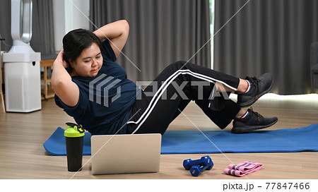 Overweight young woman watching online lessons on laptop computer and exercising at home. 77847466