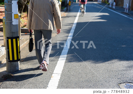 道路の端を歩く年配のシニア女性 77848932