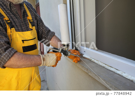 Worker using  polyurethane foam to fix window 77848942
