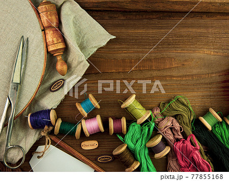 Embroidery needlework background with linen in hoop. Colorful floss thread, scissors, card tag in female hand. Handmade 77855168