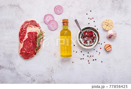 Raw Rib Eye Steak set up on white concrete background. Flat Lay of fresh raw beef steak with rosemary and spice on white shabby concrete background top view. 77856425