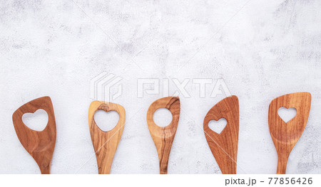 Various heart shape of wooden cooking utensils. Wooden spoons and wooden spatula on white concrete background with flat lay and copy space. 77856426