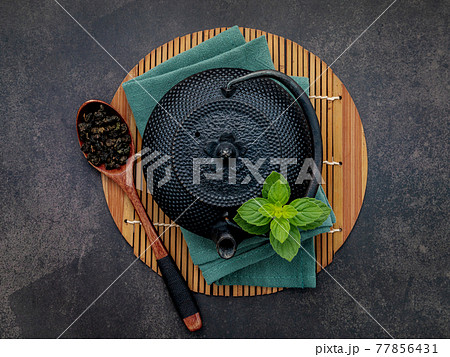 Black cast iron tea pot with herbal tea set up on dark stone background. 77856431