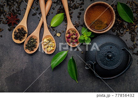 Black cast iron tea pot with herbal tea set up on dark stone background. 77856432