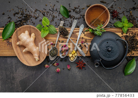 Black cast iron tea pot with herbal tea set up on dark stone background. Black cast iron tea pot with herbal tea set up on dark stone background. 77856433