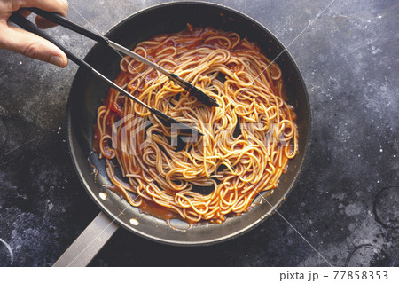 Tomato pasta is cooked in a frying pan on the kitchen background. Italian pasta background. Italian food and cuisine concept. Tomato pasta is cooked in a frying pan on the kitchen background. Italian pasta background. Italian food and cuisine concept. 77858353