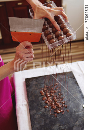 Closeup of using cake scraper to remove excess chocolate from molds into a marble table to make candy shells. Making luxury pralines and truffles at home Closeup of using cake scraper to remove excess chocolate from molds into a marble table to make candy shells. Making luxury pralines and truffles at home 77862351