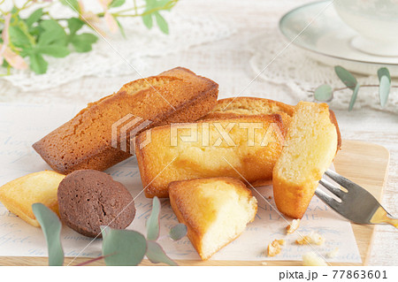 カッティングボードに置かれたいろいろなフィナンシェとティーカップ 77863601