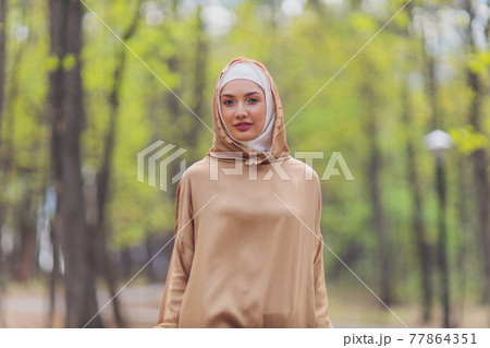 Islamic beautiful woman in a Muslim dress standing on a summer park street background forest autumn trees.world hijab day. 77864351