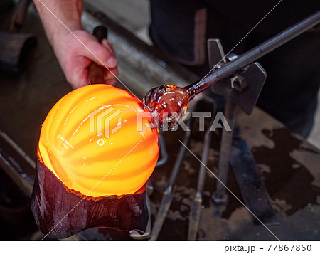 Glassblowing crafter rounds the hot-striped vase with wet woode tool Glassblowing crafter rounds the hot-striped vase with wet woode tool 77867860
