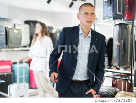 Portrait of a focused man with a travel suitcase, standing in a store Portrait of a focused man with a travel suitcase, standing in a store 77871807