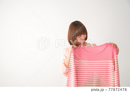 ピンク色のボーダー柄の洋服を体の前で合わせてみる若い女性 ピンク色のボーダー柄の洋服を体の前で合わせてみる若い女性 77872478