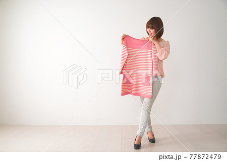 ピンク色のボーダー柄の洋服を体の前で合わせてみる若い女性 ピンク色のボーダー柄の洋服を体の前で合わせてみる若い女性 77872479