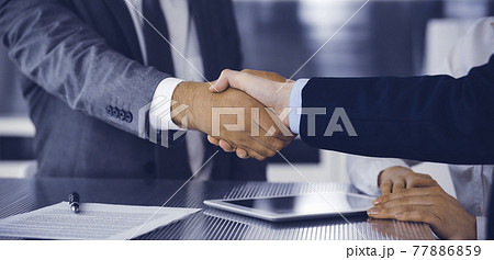 Handshake as successful negotiation ending, close-up. Unknown business people shaking hands after contract signing in modern office Handshake as successful negotiation ending, close-up. Unknown business people shaking hands after contract signing in modern office 77886859