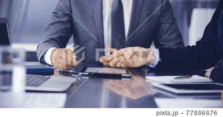 Unknown businessman using tablet computer and working together with his colleague while sits at the glass desk in modern office. Teamwork and partnership concept 77886876