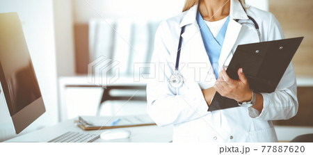 Unknown woman-doctor at work in sunny clinic. Female physician controls medication history record, close-up. Medicine concept 77887620
