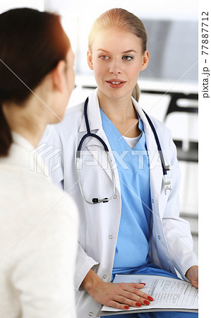 Woman - doctor consults her female patient in sunny clinic 77887712