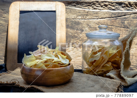 Homemade banana chips in wooden bowl and glass jar on sackcloth with vintage style. Homemade banana chips in wooden bowl and glass jar on sackcloth with vintage style. 77889097