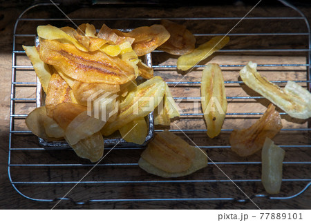 Homemade banana chips were just finished put on an iron baking rack over Rustic old wooden table. 77889101