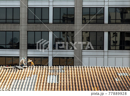 Two handyman workers repairing tiles on the damaged factory roof. Two handyman workers repairing tiles on the damaged factory roof. 77889928