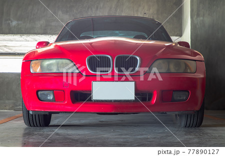In front of red Sports car parked in the Parking lot. 77890127