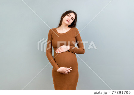 a pregnant girl who has a stomach ache stands on a colored background. isolated a pregnant girl who has a stomach ache stands on a colored background. isolated 77891709