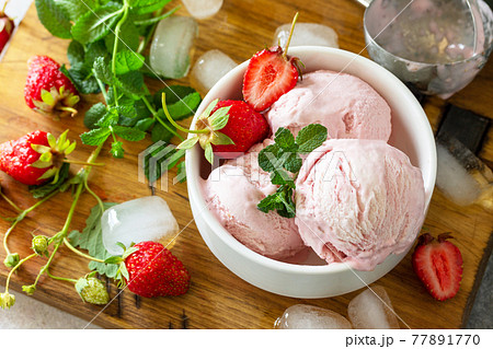 Homemade Organic Strawberry Ice Cream. Strawberry ice cream balls with mint leafon a light stone or slate table. 77891770