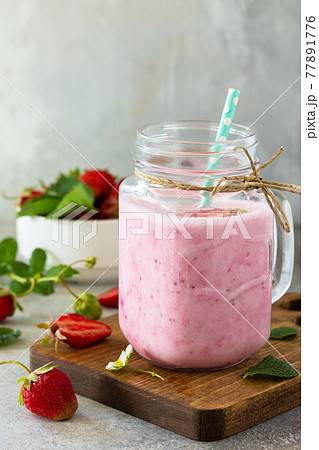 Natural detox, fruit dessert, healthy dieting concept. Strawberry fruit Yogurt smoothie or milk shake in glass jar on a light stone or slate table. Copy space. 77891776