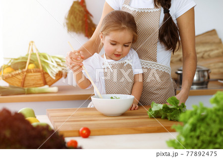 Happy woman and her daughter making healthy vegan salad and snacks for family feasting in sunny kitchen. Christmas, New year, Thanksgiving, Anniversary, Mothers Day. Healthy meal cooking concept 77892475