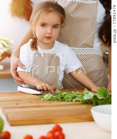Happy woman and her daughter making healthy vegan salad and snacks for family feasting in sunny kitchen. Christmas, New year, Thanksgiving, Anniversary, Mothers Day. Healthy meal cooking concept 77892476