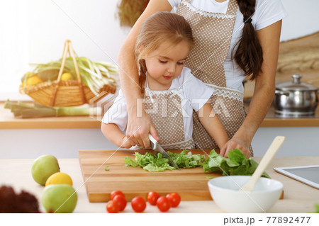 Happy woman and her daughter making healthy vegan salad and snacks for family feasting in sunny kitchen. Christmas, New year, Thanksgiving, Anniversary, Mothers Day. Healthy meal cooking concept 77892477
