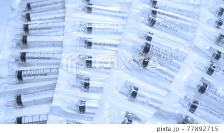 Medical syringes in a package. A bunch of unused, packaged syringes.Many new syringes lie strewn on a flat surface. 77892715