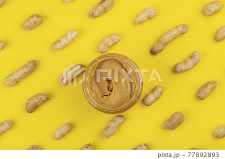 Bowl of peanut butter and scattered peanuts on yellow background 77892893