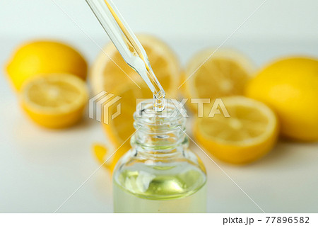 Pipette dripping oil in bottle against fresh lemons Pipette dripping oil in bottle against fresh lemons 77896582
