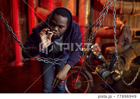 Drug addict man smokes a cigarette in den 77896949