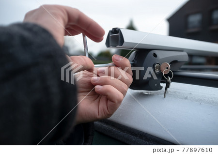 Hands with a screwdriver installs attachments for the trunk or cargo box on the roof of the car. Hands with a screwdriver installs attachments for the trunk or cargo box on the roof of the car. 77897610