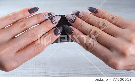 Female hand with beautiful manicure nails in the form of chocolate candies, holding an unrolled bar 77900618