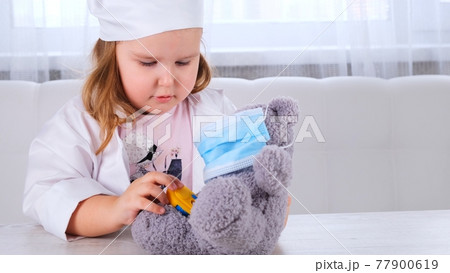 little girl plays a doctor, measures the temperature. Happy child little doctor examines a teddy little girl plays a doctor, measures the temperature. Happy child little doctor examines a teddy 77900619