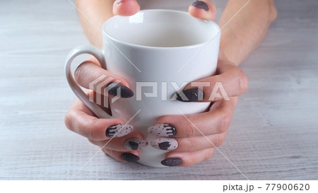 Beautiful manicured nails in the form of chocolate candies on female hands close-up and a cup of 77900620