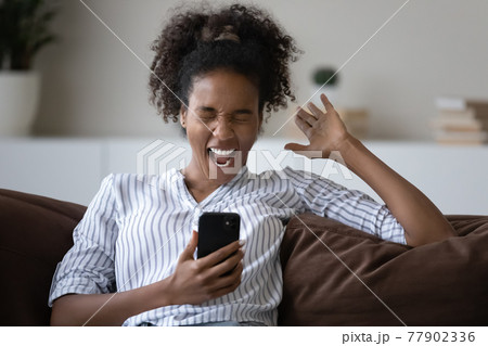 Overjoyed young african woman celebrating online lottery win. 77902336