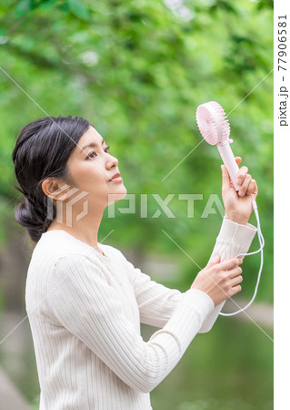 新緑の中でハンディファンを持って涼んでいるビジネスウーマン  77906581