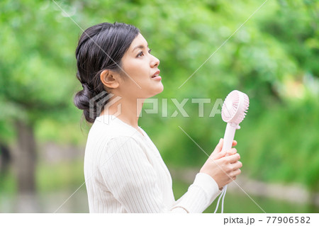 新緑の中でハンディファンを持って涼んでいるビジネスウーマン  77906582